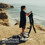 Surfer changing out of a wetsuit under the SAAL poncho on a coastal cliff