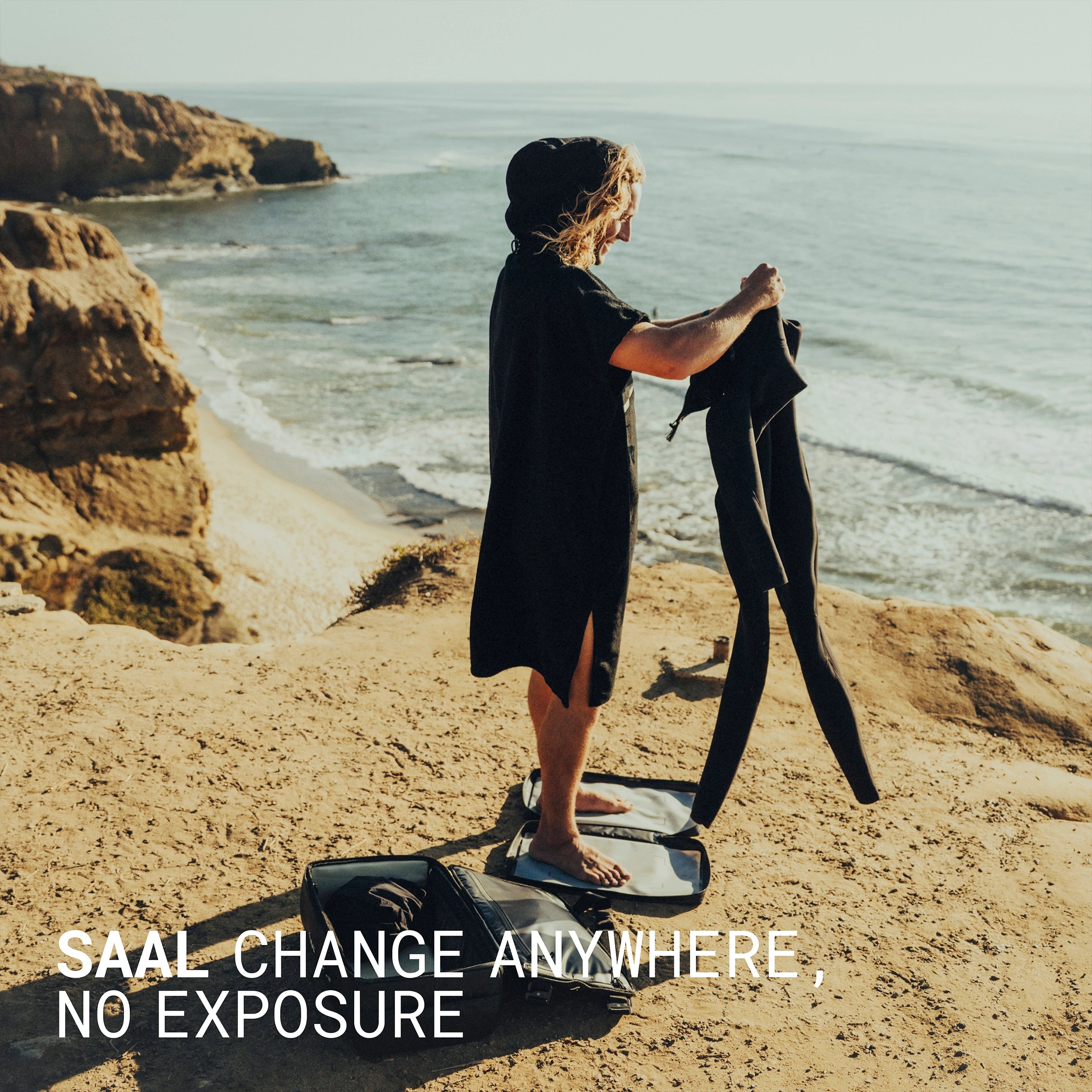Surfer changing out of a wetsuit under the SAAL poncho on a coastal cliff