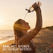 Woman rinsing off at the beach at sunset with the SAAL Surf Rinse portable shower